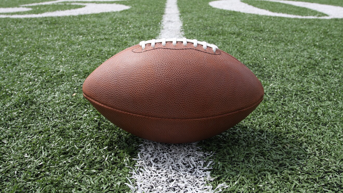 An image of a football sitting on top of a green football field with white yard markings.