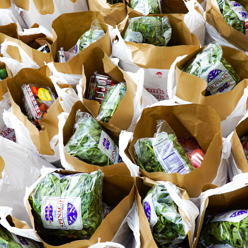 Overhead photograph of dozens of bags filled with fresh strawberries, spinach, and other groceries.