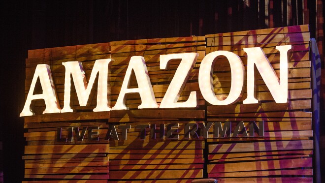 亚马逊在纳什维尔的活动舞台上写着“莱曼现场直播”。这个标识有三个面板宽,每个面板都由水平的木板拼接而成。上面有点亮的字母拼成“亚马逊”(Amazon),下面写着“住在莱曼”(Live at the Ryman)。