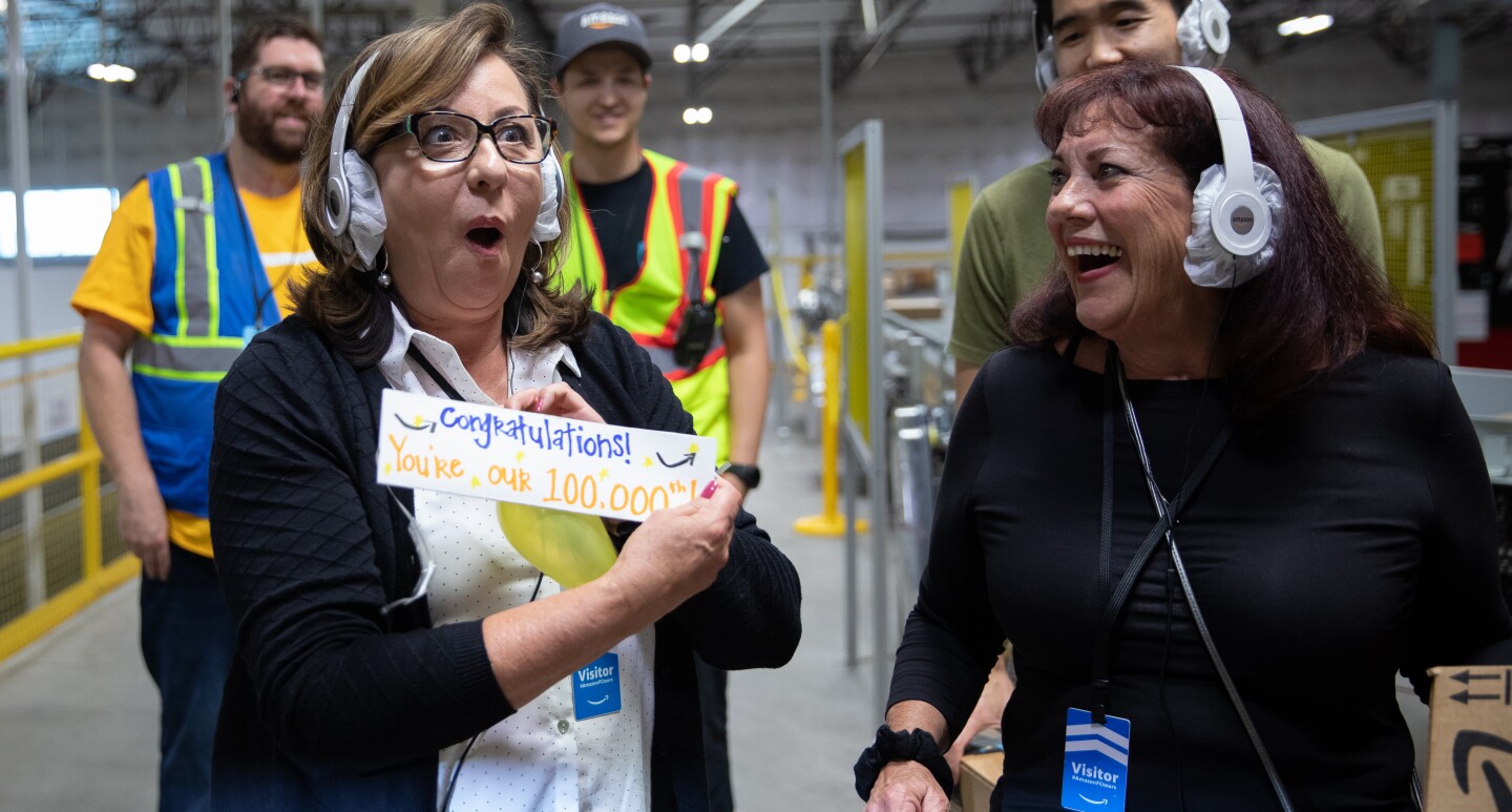 A woman on a tour is surprised and excited to learn that she is the 100,000th person to take a tour as she holds a special card that say congratulations