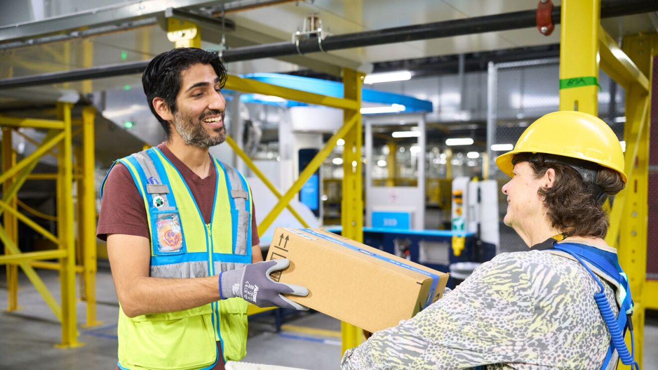 Warehouse workers exchanging package, one in safety vest, other in hard hat