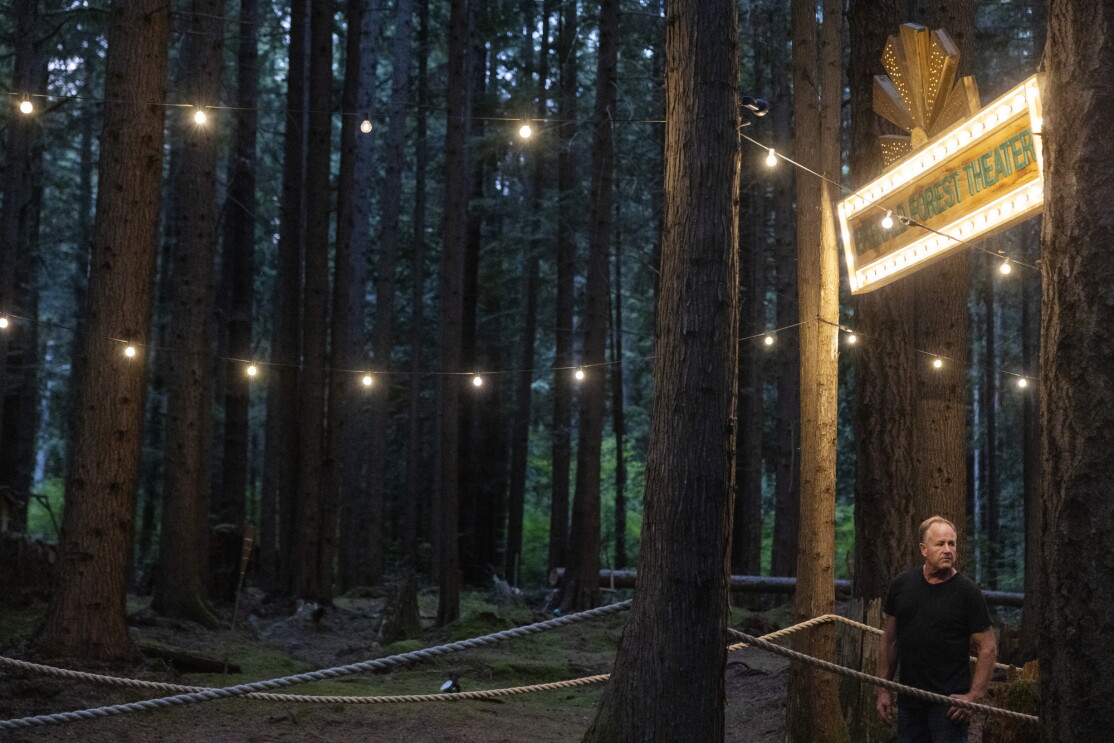 A man stands below a sign in a forest.
