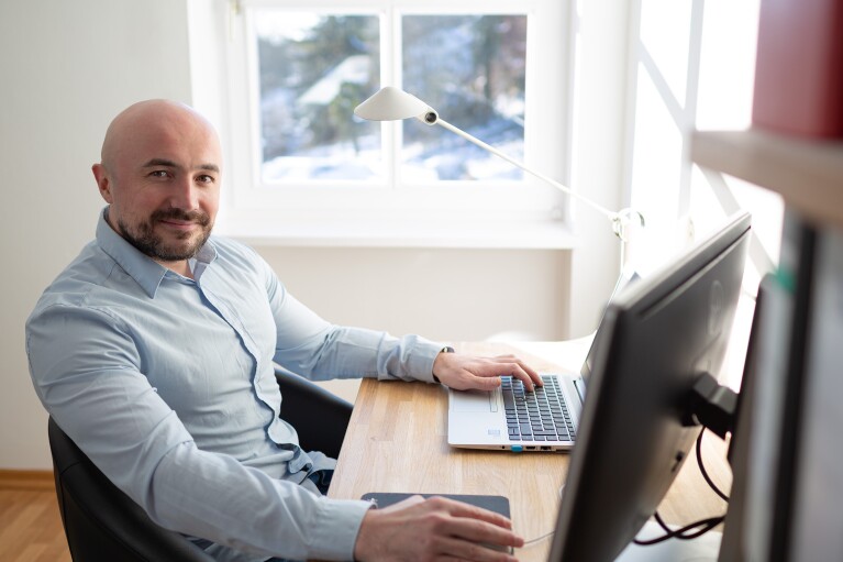 Ein Mann mit hellblauem Hemd sitzt an einem Schreibtisch und schaut in die Kamera.