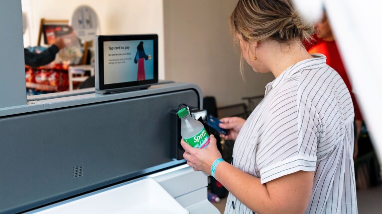 Self-service kiosk with 'Tap card to pay' screen and customer purchasing Sprite, just walk out technology