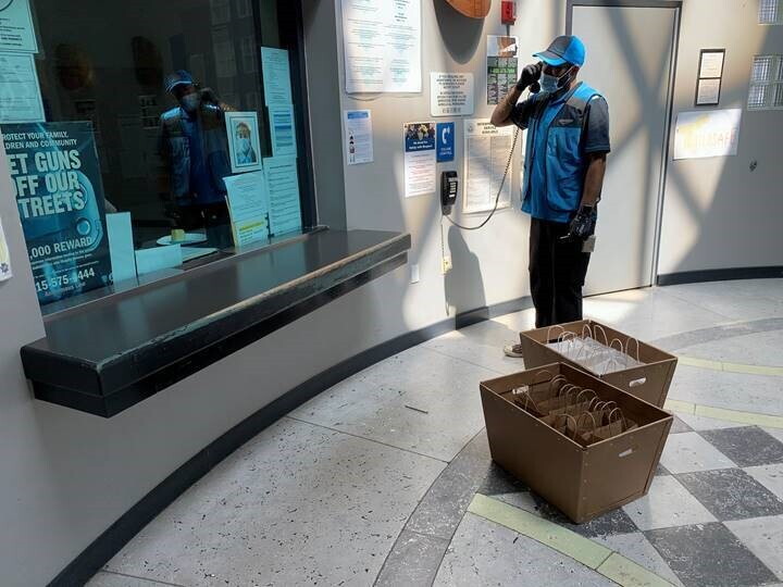 A delivery driver tasks on a landline phone while standing near two boxes filled with individual bags. 