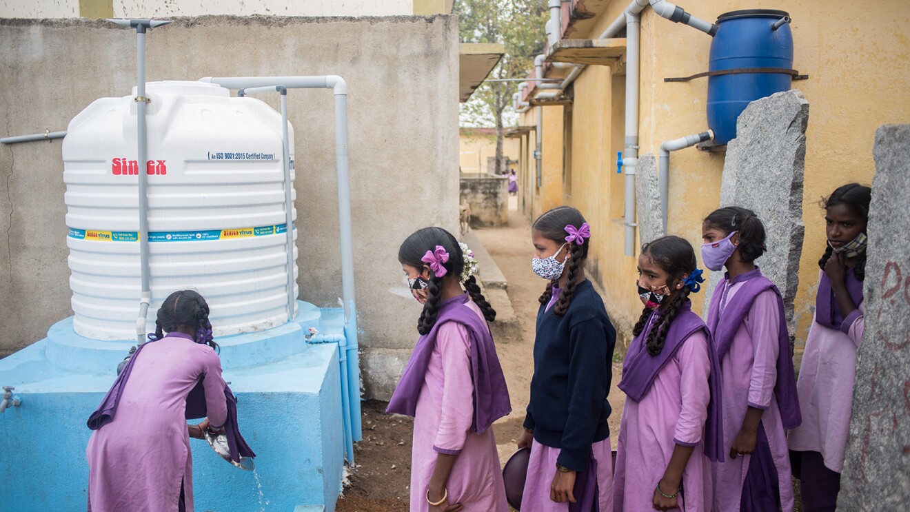 School students washing their hands and plates with soap and clean water at the water storage tank with a capacity of 2500 liters connected to a Rain Water Harvesting (RWH) constructed by WaterAid India inside the complex of Zilla Parishid High School.