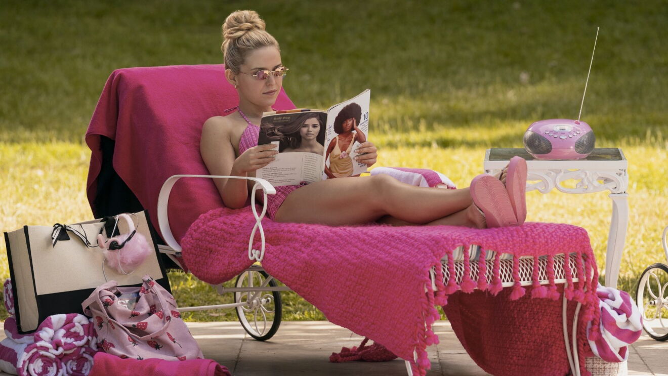 Still image from 'Elle' Season 1, actress in pink bikini reading magazine while lounging on pink chair outdoors with matching accessories