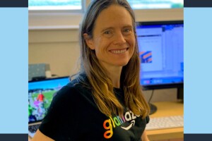 Amazon robotics employee Heidi smiles as she sits at her desk wearing a glamazon shirt.