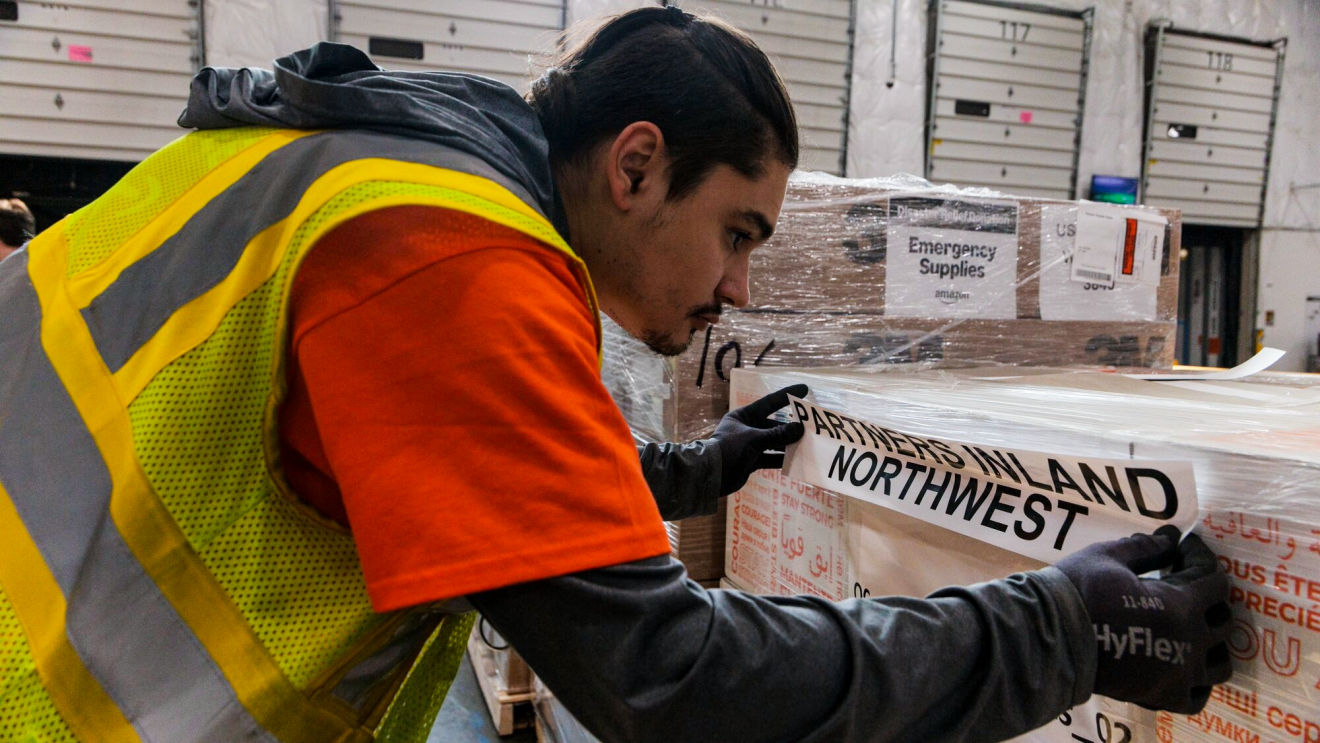 An Amazon employee wears a yellow safety vest and packages up disaster relief items.