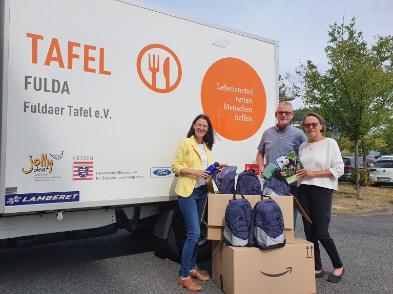 Amazon Volunteers mit Amazon Boxen und blauen Schulrucksäcken vor einem Laster der Fuldaer Tafel.