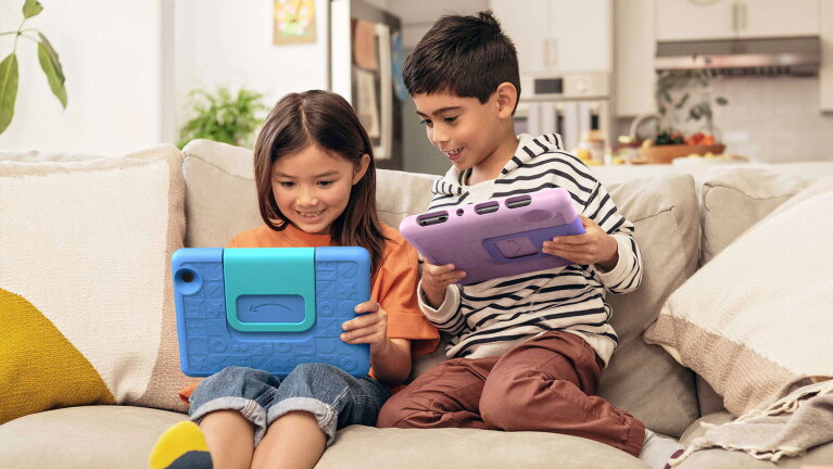 An image of two children using their Amazon tablets while sitting on the sofa.
