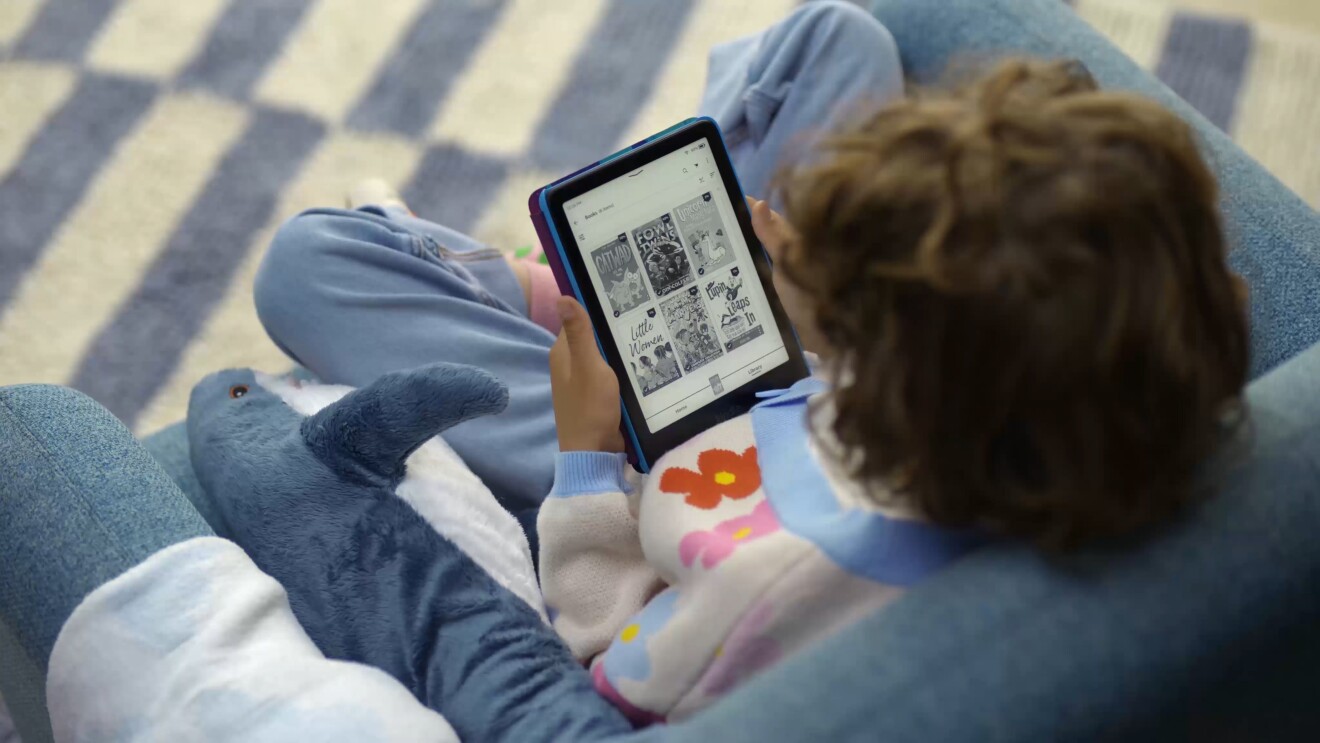 A child sat in an armchair holding a Kindle Paperwhite Kids
