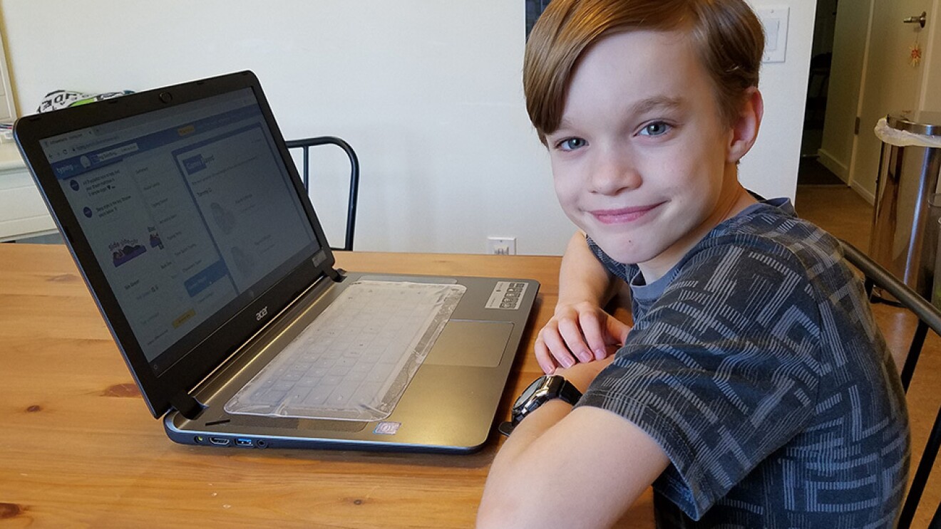 An elementary age student sits with their laptop computer in their home