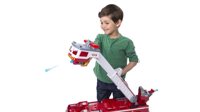 爪子巡逻消防车玩具有2英尺高可扩展的阶梯,迷你车,光和声音,高压水枪发射器。一个男孩跪在玩具,探索消防车的功能。