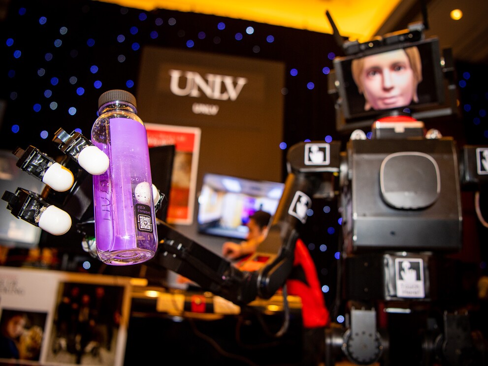 An image of a robot holding a water bottle. There is a sign that says "UNLV" in the background.