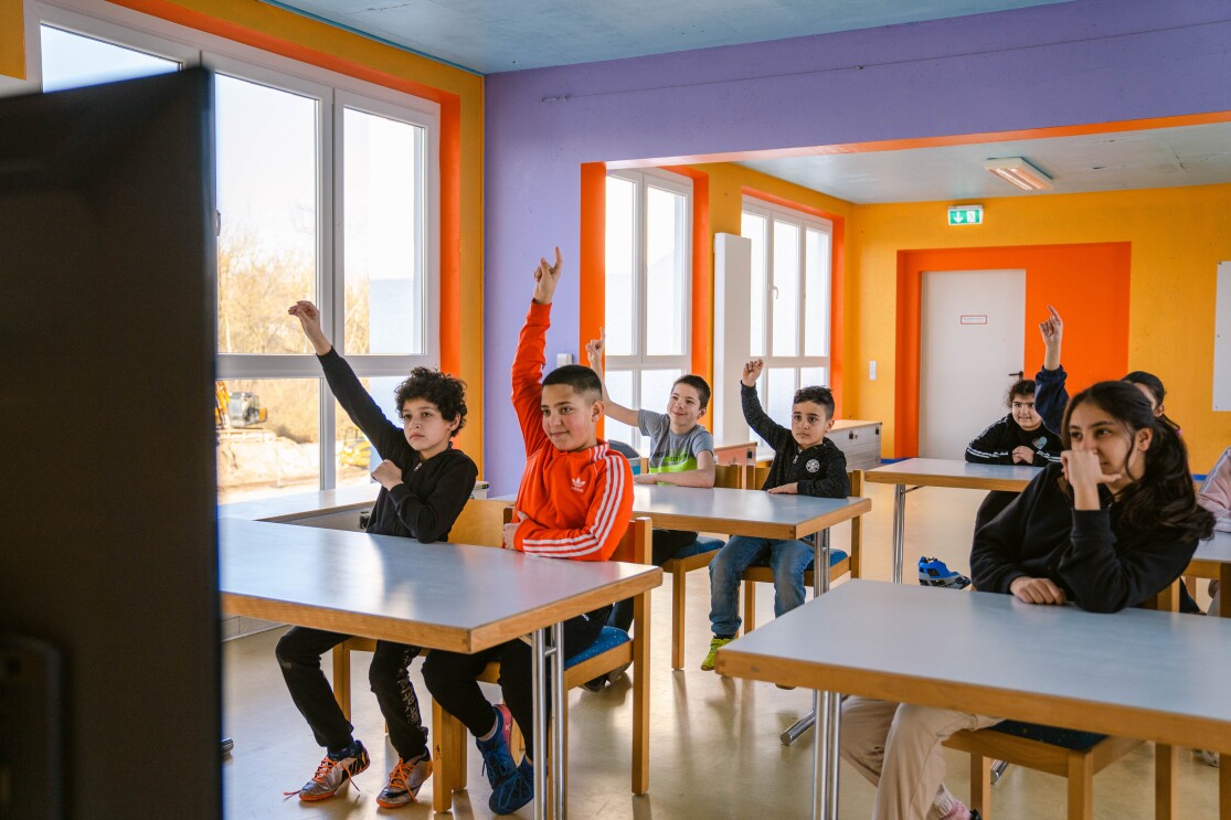 Kinder der Arche verfolgen in einem Klassenzimmer auf einem Bildschirm die virtuelle Tour. Mehrere Kinder melden sich.