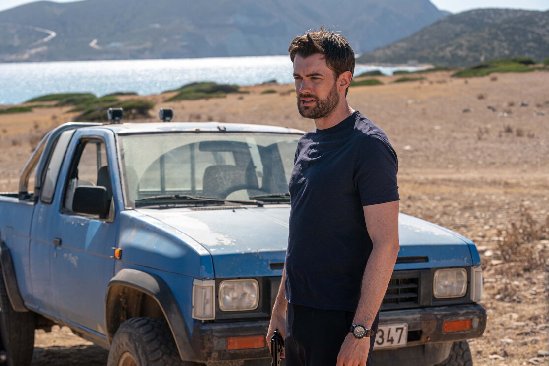 A pensive looking man stands next to an old car