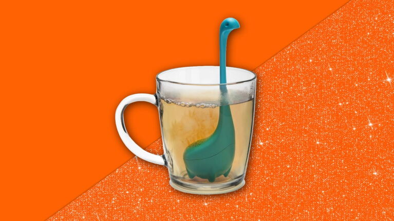Dinosaur-shaped tea infuser in a glass mug on orange background
