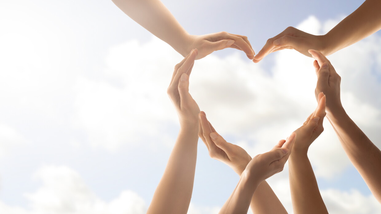 Image of various hands forming a heart, against a clear blue sky.