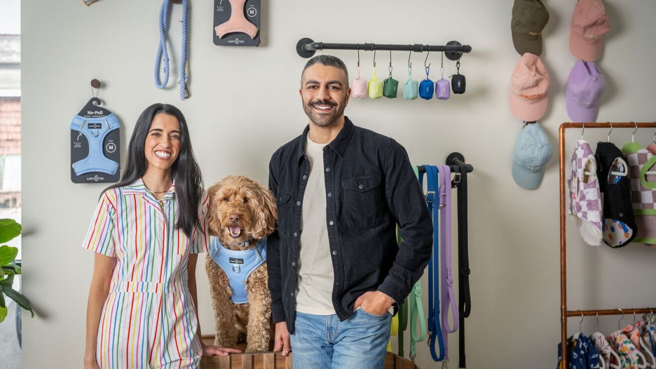 Ashley and Ahmed El Shourbagy, co-founders, Lucy & Co. standing in front of dog accessories. A dog is sitting between them.