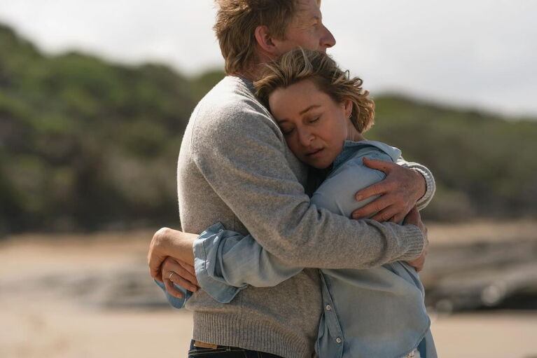 Couple embracing tightly on a beach with hills in background