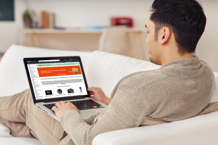 Amazon_Graphic_Pre Loved: Ein Mann halb liegend auf der Couch mit einem Laptop, der auf seinen Oberschenkeln liegt.