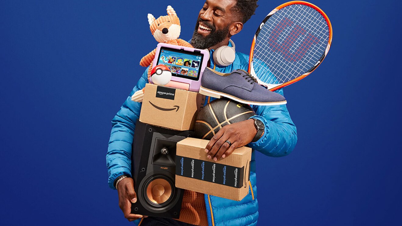 an image of a man holding several amazon boxes and various items like a basketball, a tennis racket, a speaker, and a stuffed animal. There is a blue background behind him.