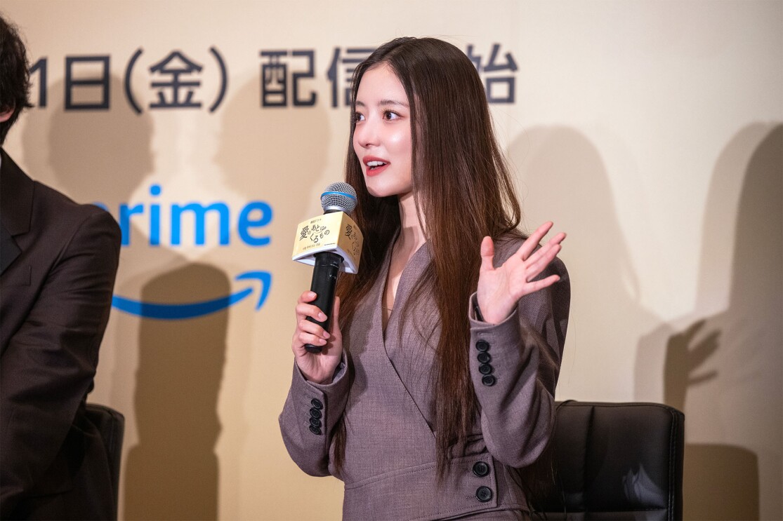 茶色のドレスを着ている女性がマイクを持ち話している。