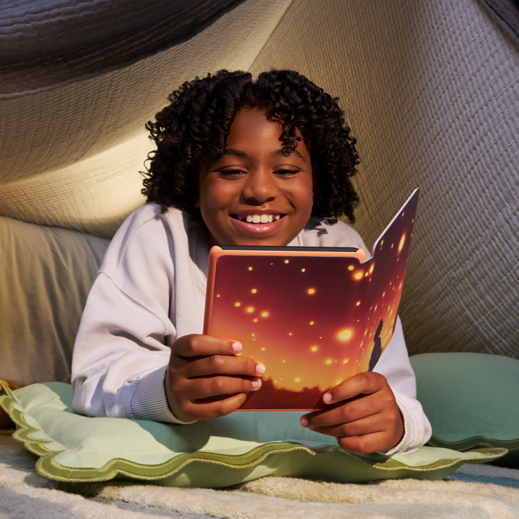 Child smiling and reading Kindle Colorsoft inside a blanket fort 