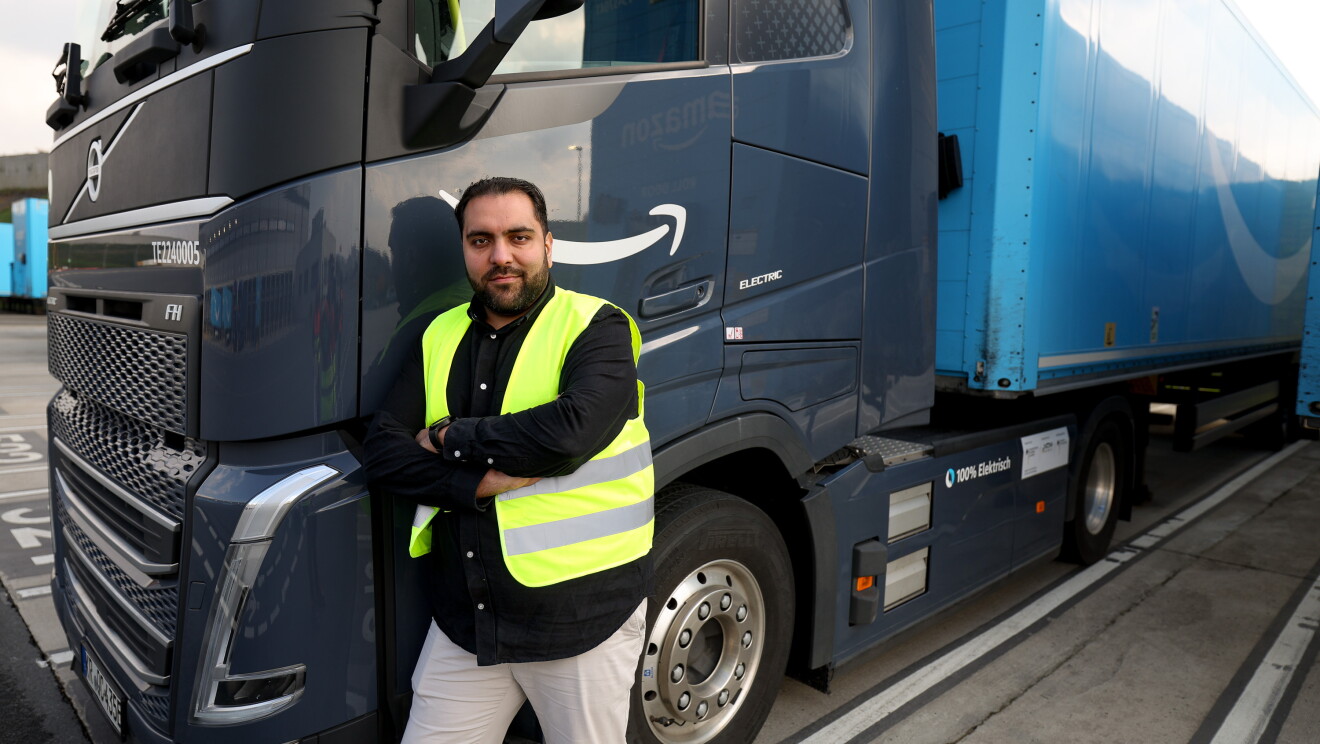 Samir leans against the front side of an electric truck
