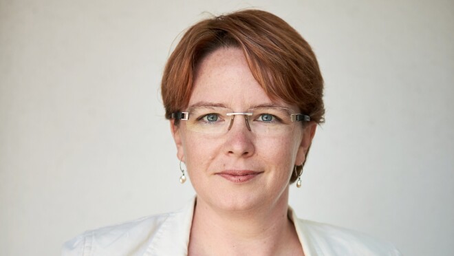 一个女人微笑的头像照片在白色背景前,身穿白色上衣,眼镜。