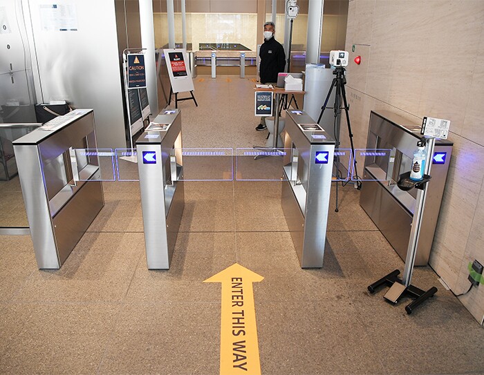 入館ゲートの横に消毒液とサーモグラフィカメラが設置されている。警備員がこちらをみている