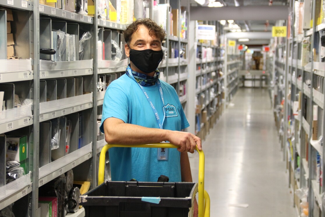 Ein Mitarbeiter mit Maske und blauem T-Shirt in einem Regalgang.