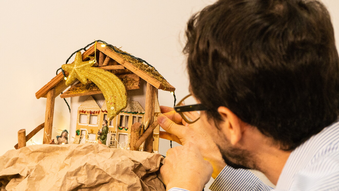 Fernando Poucell es arquitecto y empezó a trabajar en Amazon hace tres meses. En la foto se ve Fernando de perfil colocando un portal de Belén hecho a mano con maderas, luces y cartones. Él tiene el pelo negro corto, lleva barba y una gafas. 