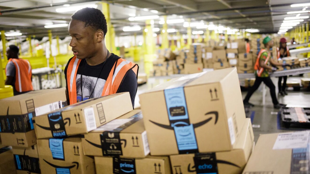 A man wears an orange safety vest and works in an Amazon fulfillment center.