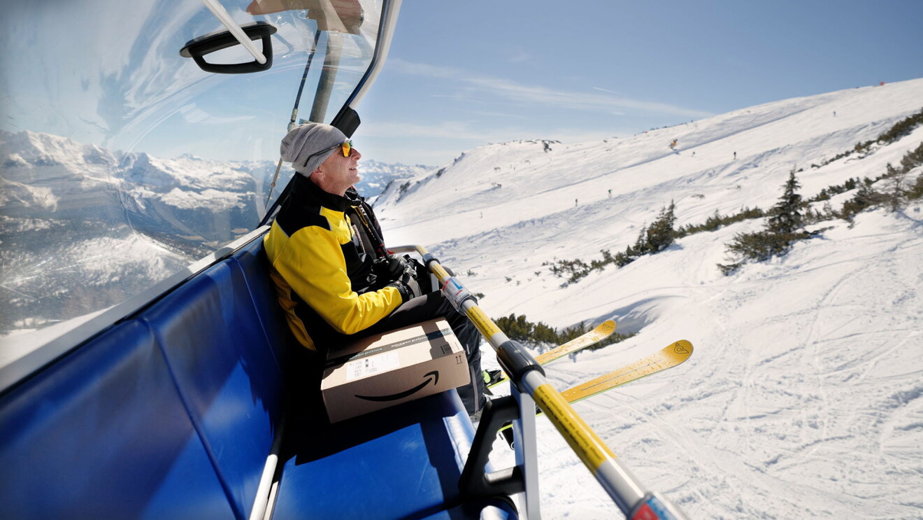 Helmut Edelmaier rides the gondola up the mountain with an Amazon package on the seat next to him.