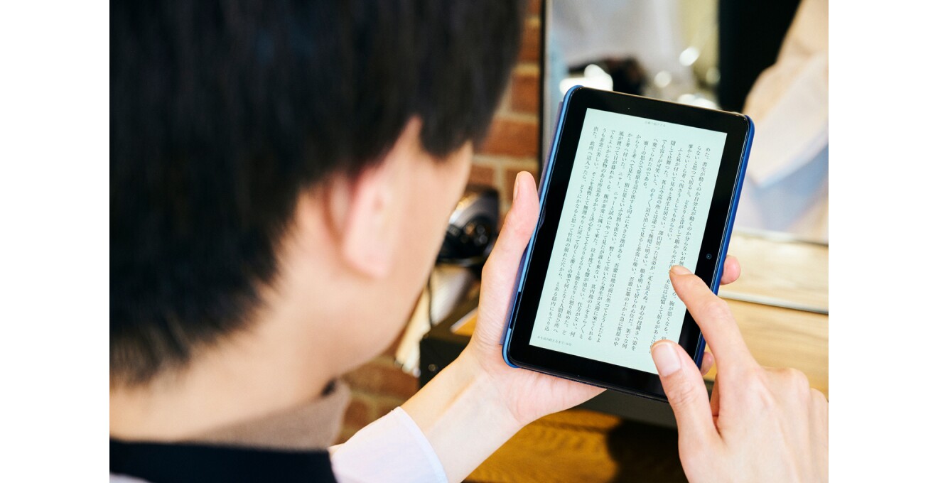 美容室でケープから手を出しFire 7で読書をする写真
