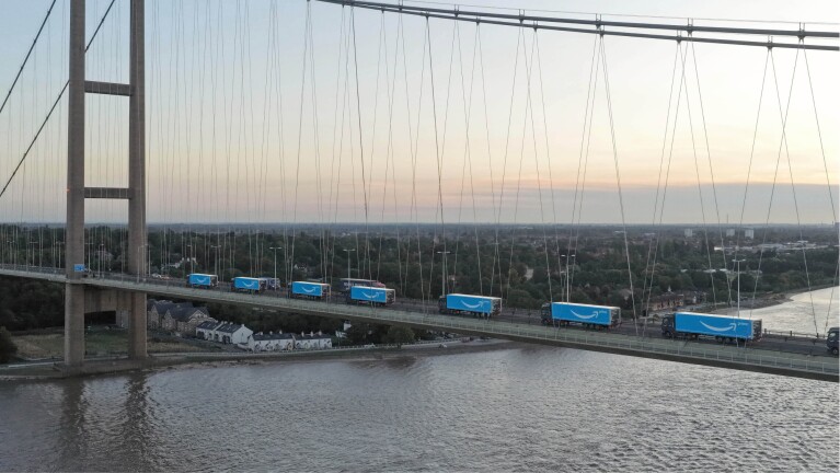 Amazon delivery trucks crossing suspension bridge over river at sunset