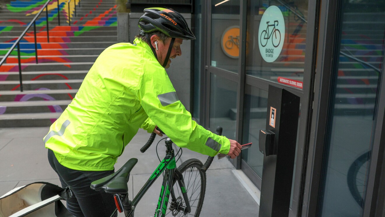 An Amazon employee badging into the bike garage wearing a neon jacket and riding his bike. 