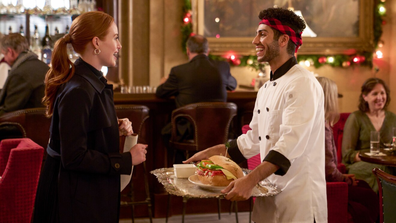 A still of Madelaine Petsch and Mena Massoud in Amazon Freevee's original holiday movie, 'Hotel for the Holidays.'