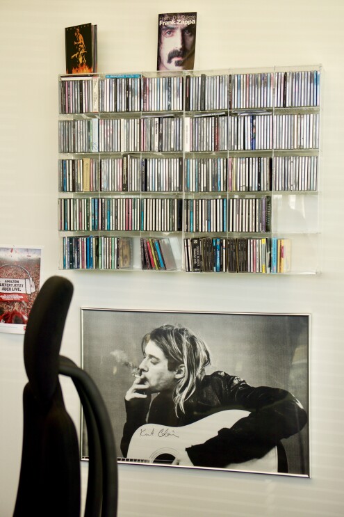 Eine Bürowand zeigt von unten nach oben: ein handsigniertes Porträt von Kurt Cubain, ein gefülltes CD-Regal und rechts: einen roten Fußball-Fanschal, der an der Wand befestigt wurde.