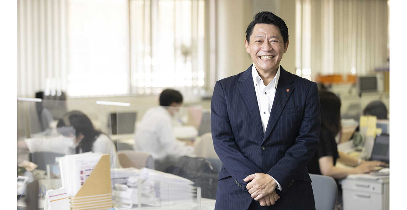 職員の方がデスクワーク中の事業所で笑顔の滑田さん