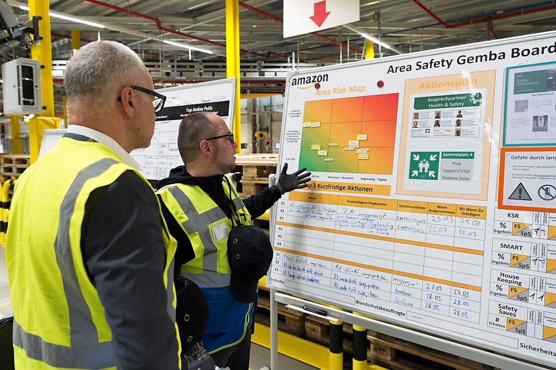 Emmanuel Frank weist auf eine große Tafel mit Grafiken und handschriftlichen Hinweisen. Neben ihm steht ein grauhaariger Mitarbeiter