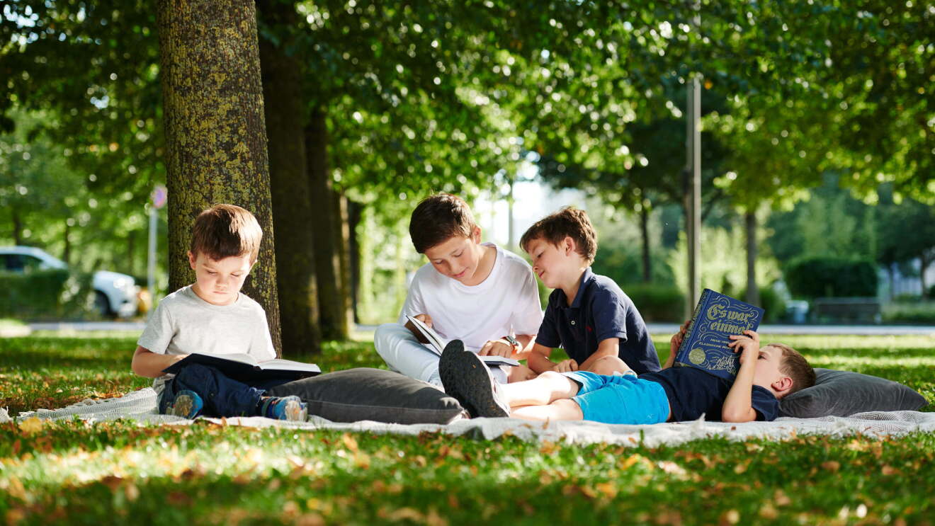 Kinder sitzen im Wald auf einer Picknickdecke und lesen