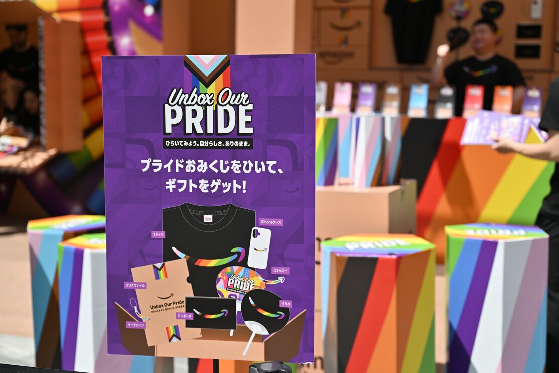 プライドおみくじをひいて、ギフトをゲットと書かれた紫色のパネル。背景にレインボーカラーのおみくじの箱が並んでいる