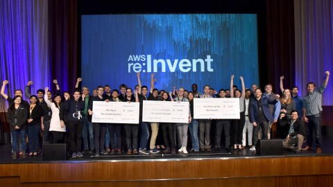 数十名学生排队参加AWS Re:Invent课程。三组学生拿着奖金支票。"width=