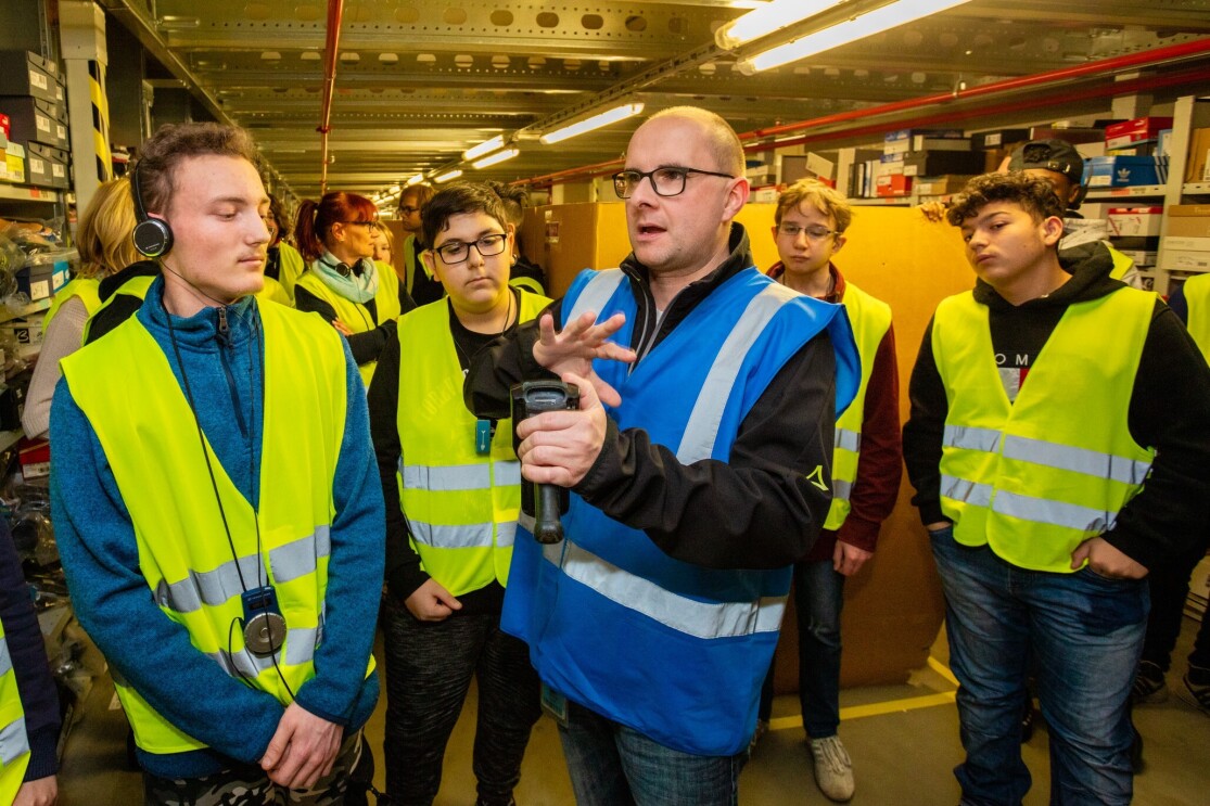 Ein Mann mit Brille und blauer Sicherheitsweste hält einen Scanner in der Hand. Ein Gruppe von SchülerInnen hat sich um ihn versammelt und hört ihm zu.