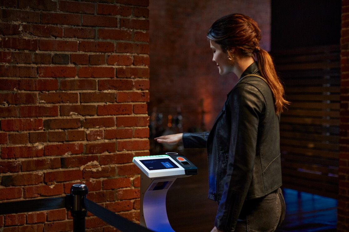 A woman holds her palm over a Amazon One device at a concert venue.