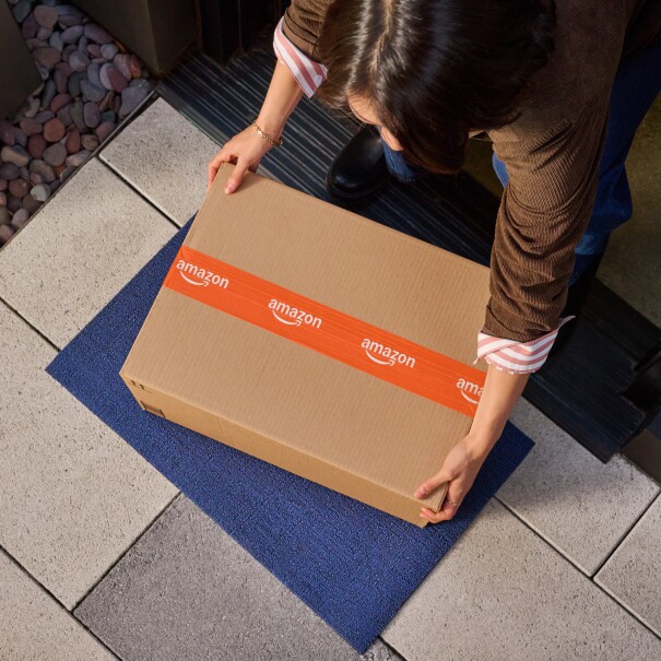 From a bird''s eye perspective, a woman bending down to pick up an Amazon box at the front door of her home.