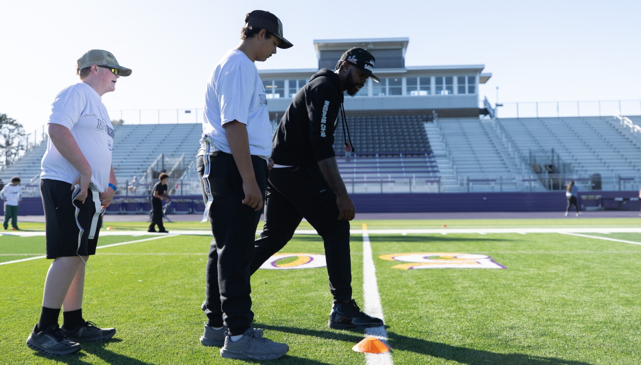 Former Seahawks wide receiver Sidney Rice leads students in an agility drill on a football field.